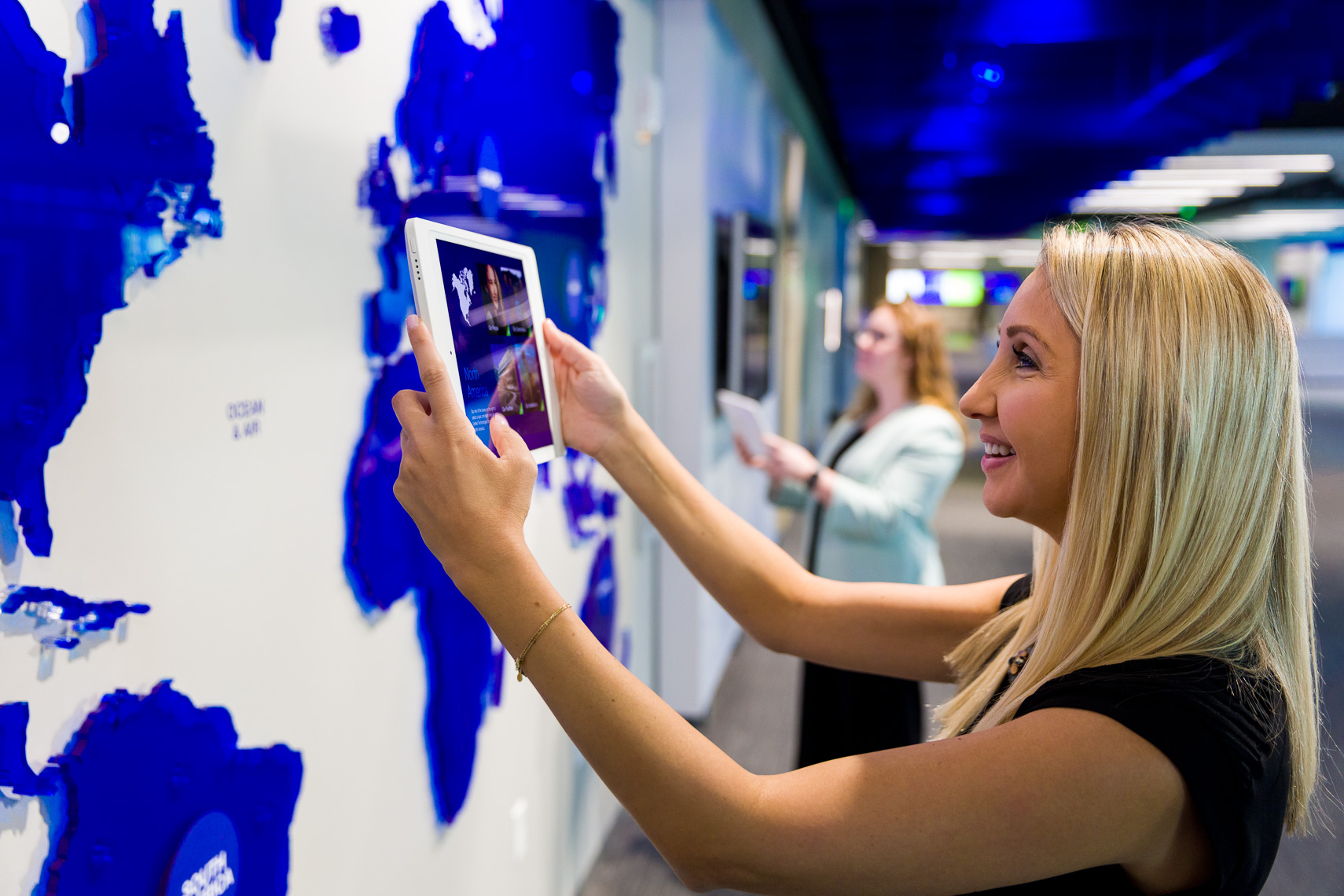 Two women interact with a technology wall and tablets